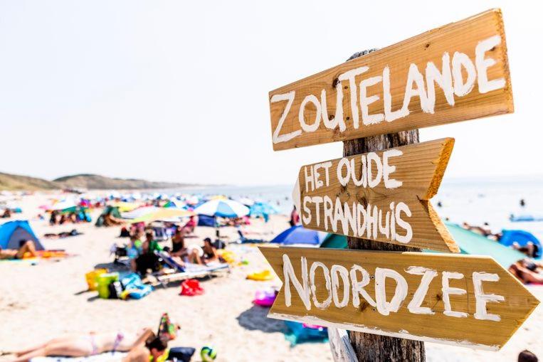 a pole with signs on a beach with people at Dulce Tierra - vakantiewoning in Zoutelande