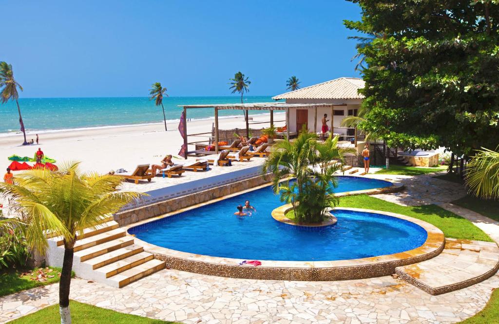 a swimming pool next to a beach with people laying on the beach at Windtown Beach Hotel in Cumbuco