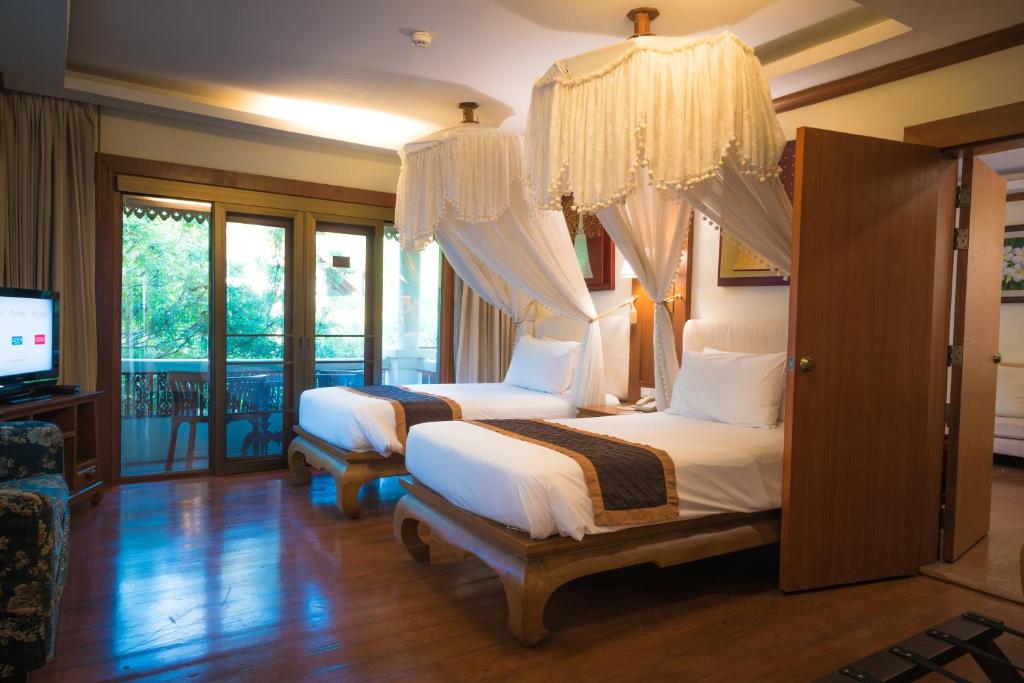 a bedroom with two beds and a tv and windows at Khum Phaya Resort & Spa Boutique Collection in Chiang Mai