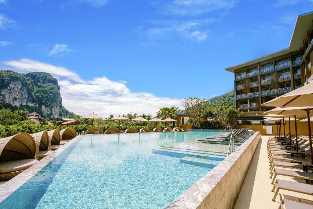 a pool at a hotel with chairs and mountains in the background at Centara Life Phu Pano Krabi-SHA Plus in Ao Nang Beach