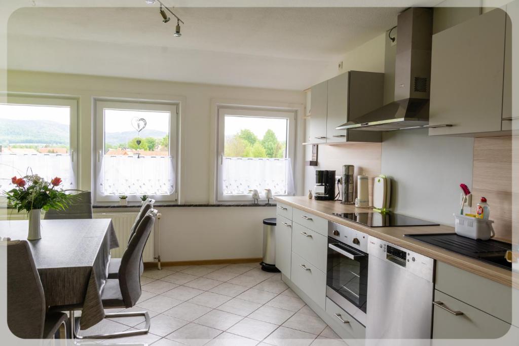 uma cozinha com armários brancos, uma mesa e janelas em Ferienwohnung Probst em Seesen