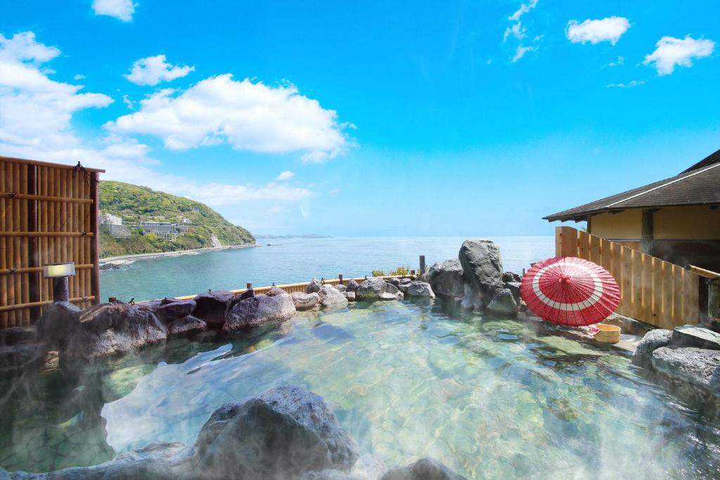 - une piscine avec des rochers et un parasol dans l'établissement Ooedo Onsen Monogatari Hotel Suiyotei, à Atami