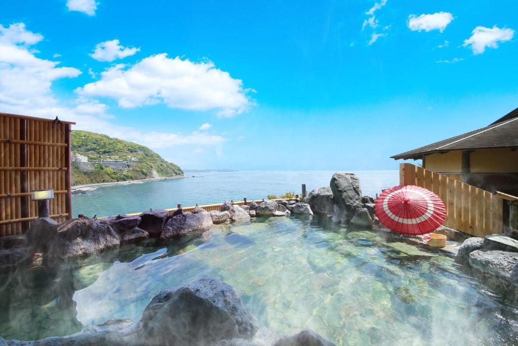 ein Pool mit Steinen und einem Sonnenschirm in der Unterkunft Ooedo Onsen Monogatari Hotel Suiyotei in Atami
