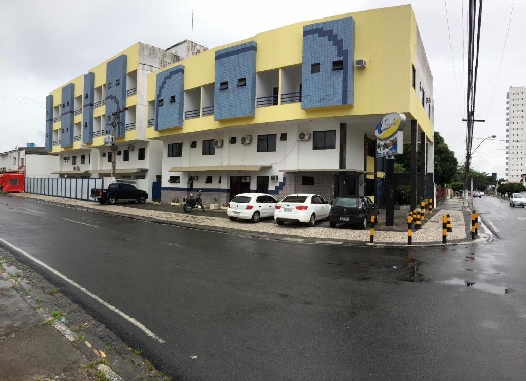 a building with cars parked on the side of a street at Hotel Kalilândia in Feira de Santana