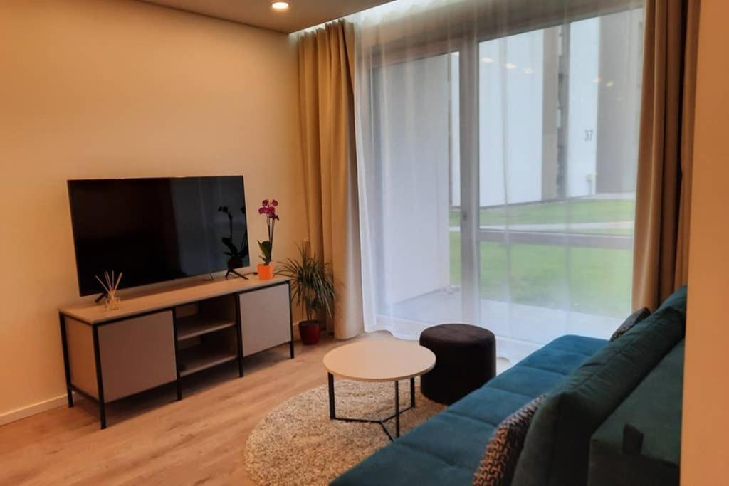a living room with a blue couch and a large window at Apartamentai Giluzes Rivjera in Vilnius