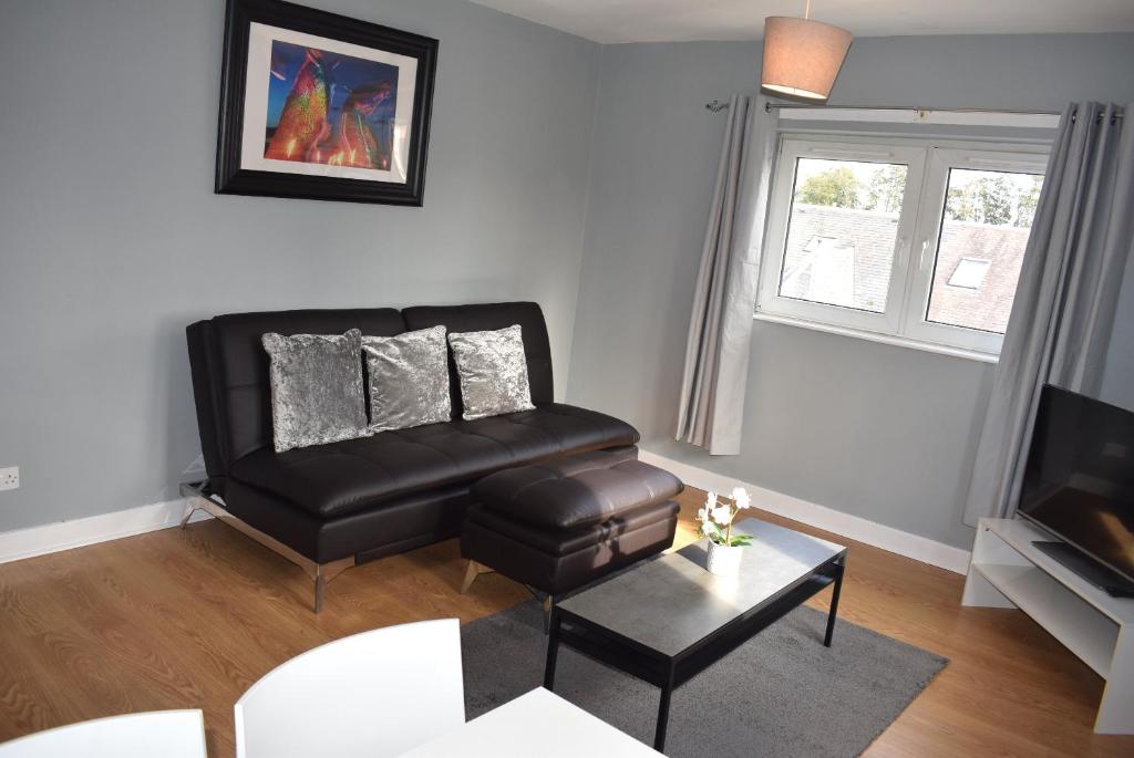 ein Wohnzimmer mit einem schwarzen Ledersessel und einem TV in der Unterkunft Kelpies Serviced Apartments- Campbell in Pumpherston