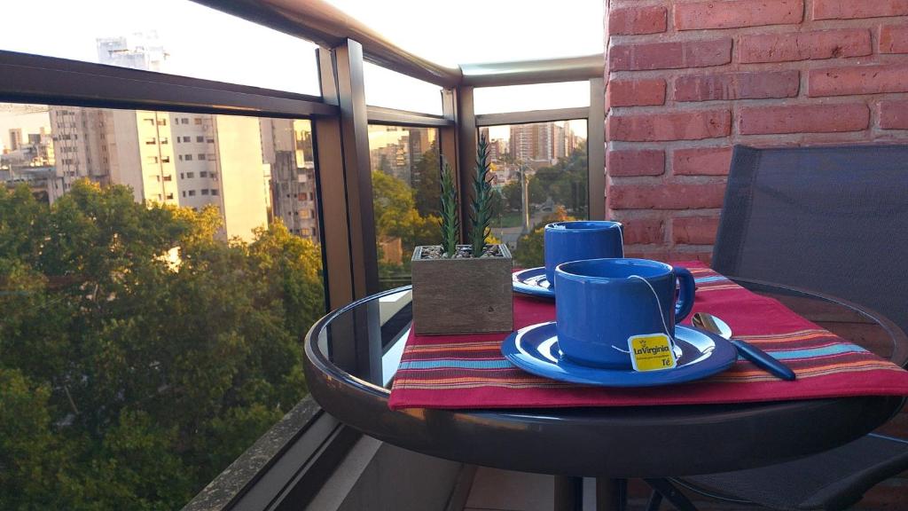 uma mesa com duas chávenas azuis e pratos numa varanda em Bello 9no piso en Plaza Italia (con cochera) em La Plata