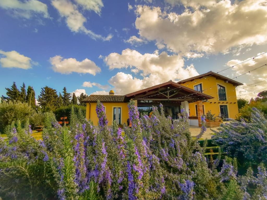 a garden with purple flowers in front of a yellow house at Country House Erba Regina in Frascati