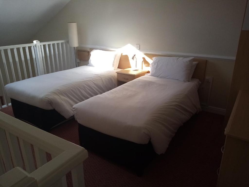 two beds in a hotel room with a light on at Moreton Park Hotel in Chirk