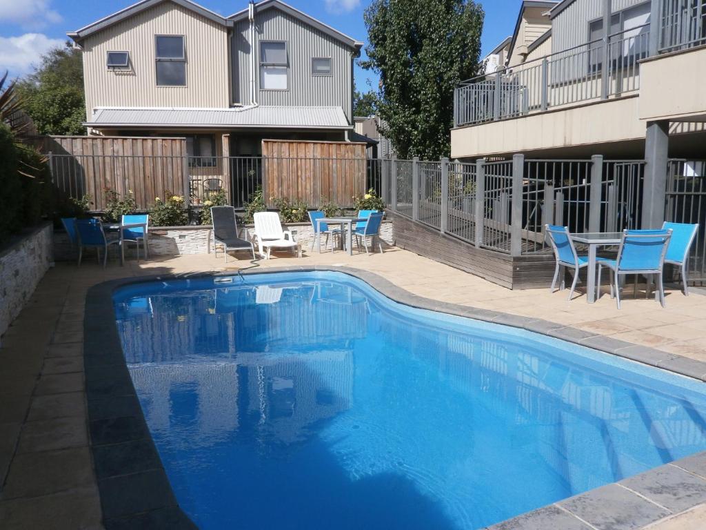 a swimming pool with blue chairs and a house at Sovereign Views Apartments in Ballarat