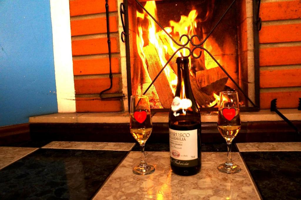 una botella de vino y 2 copas de vino junto a la chimenea en Pousada Amor Perfeito, en Visconde De Maua