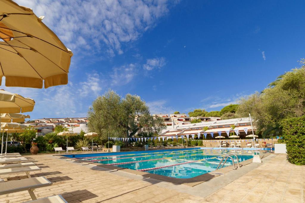 a pool at a hotel with an umbrella and chairs at Residence Solemaremma in Castiglione della Pescaia