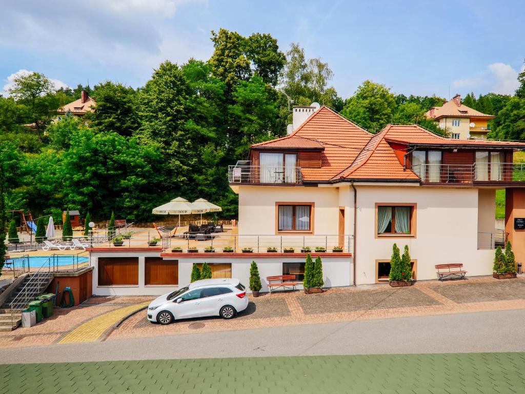 Two-story villa with terracotta roof, white parked car, terrace and surrounding greenery.