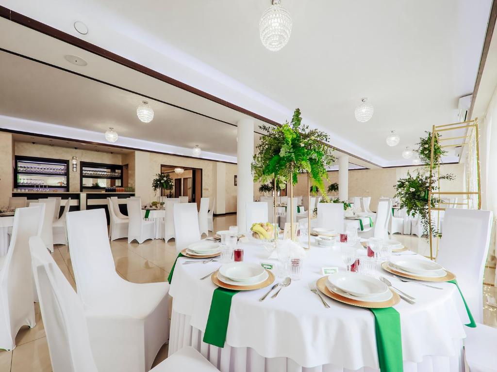 Elegant banquet hall with round table settings, green napkins, white chairs, lush floral centerpieces.