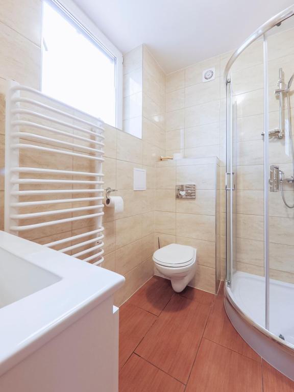 Bright tiled bathroom with corner shower, wall-mounted toilet, and white towel radiator.