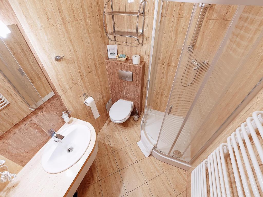 Compact beige-tiled bathroom featuring sink, wall-mounted toilet, and curved glass shower enclosure.
