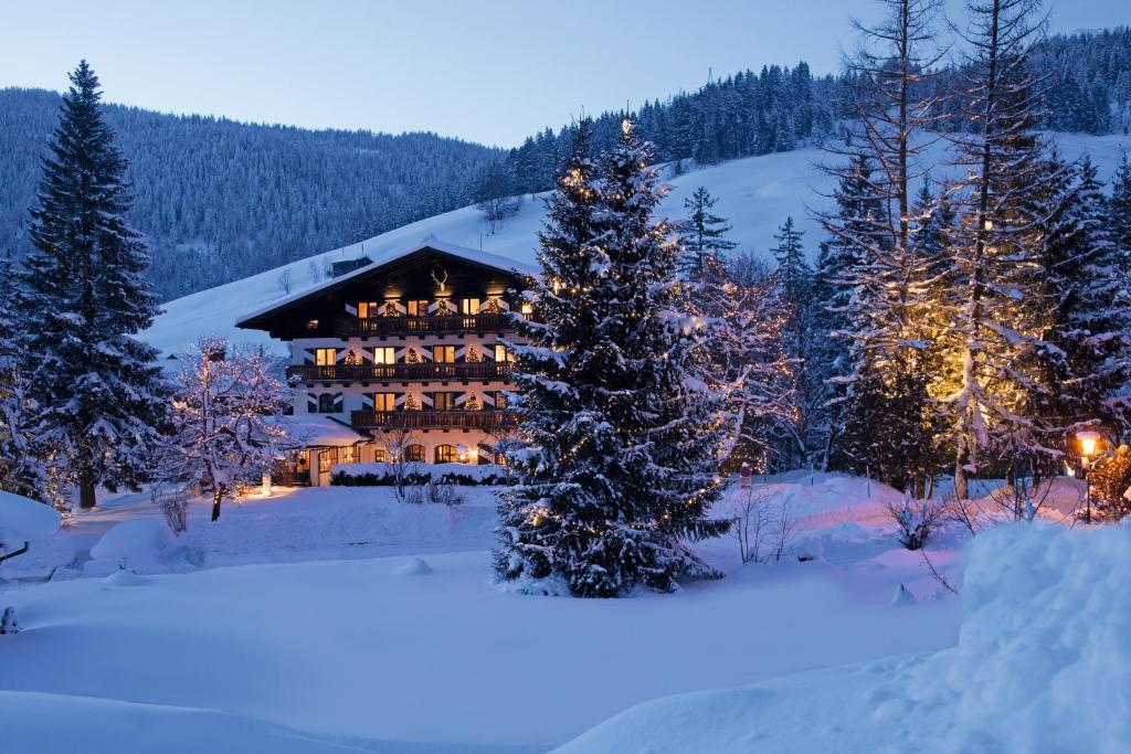 a log cabin in the snow with christmas lights at House of Hütter - Wachtelhof Hotel & Spa in Maria Alm am Steinernen Meer