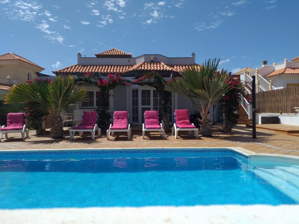 a swimming pool with chairs and a house at Villa Rochelle in Caleta De Fuste