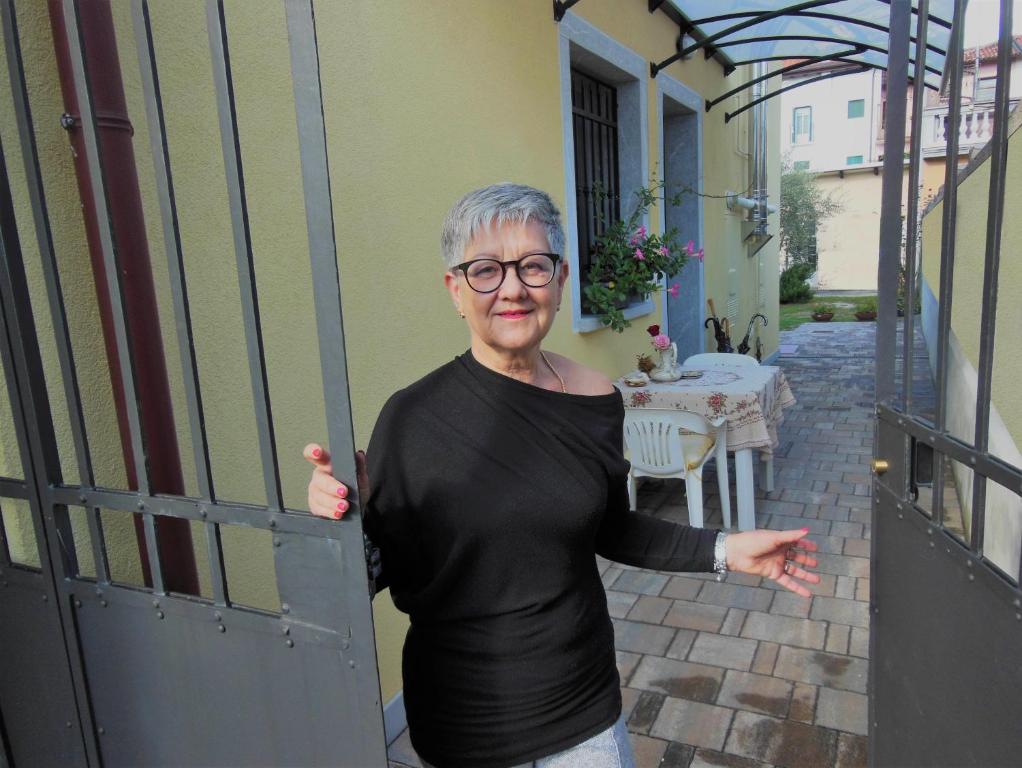 une femme âgée tenant une porte ouverte sur une terrasse couverte dans l'établissement AVD - La Nuova Casa di Nonna, à Udine