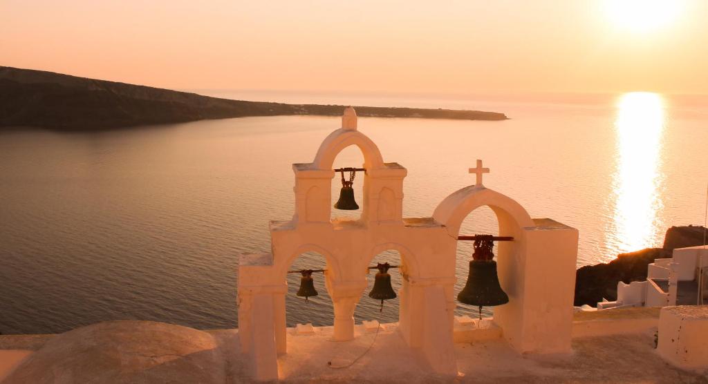 a church with bells and a cross next to the water at Casa Sigala sunset in Oia