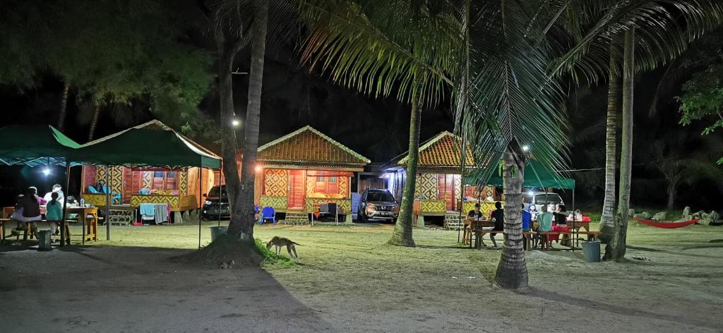 un complexe avec des tables, des chaises et des palmiers la nuit dans l'établissement Pantai Camara Homestay, à Rorahmakan