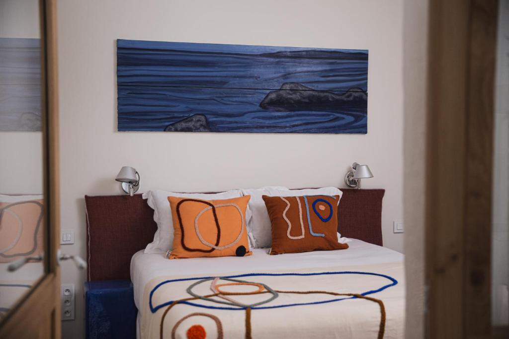 a bed with orange pillows and a painting on the wall at Suites The Marcel in Sète