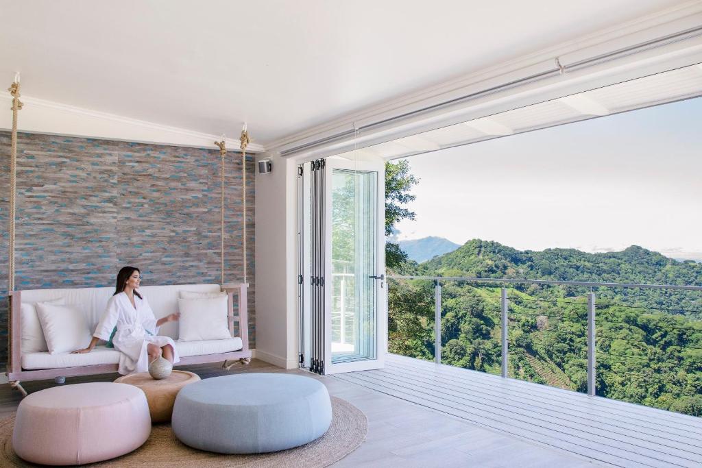a woman sitting on a couch in a room with a large window at The Retreat Costa Rica - Wellness Resort & Spa in Atenas