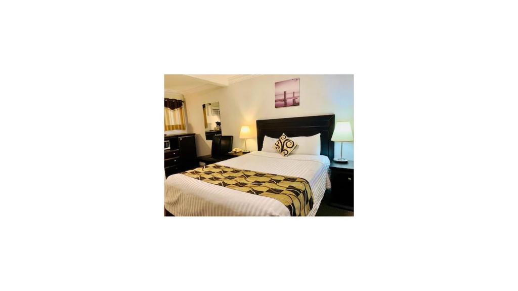um quarto de hotel com uma cama com lençóis brancos em Traveler's Motel Penticton em Penticton