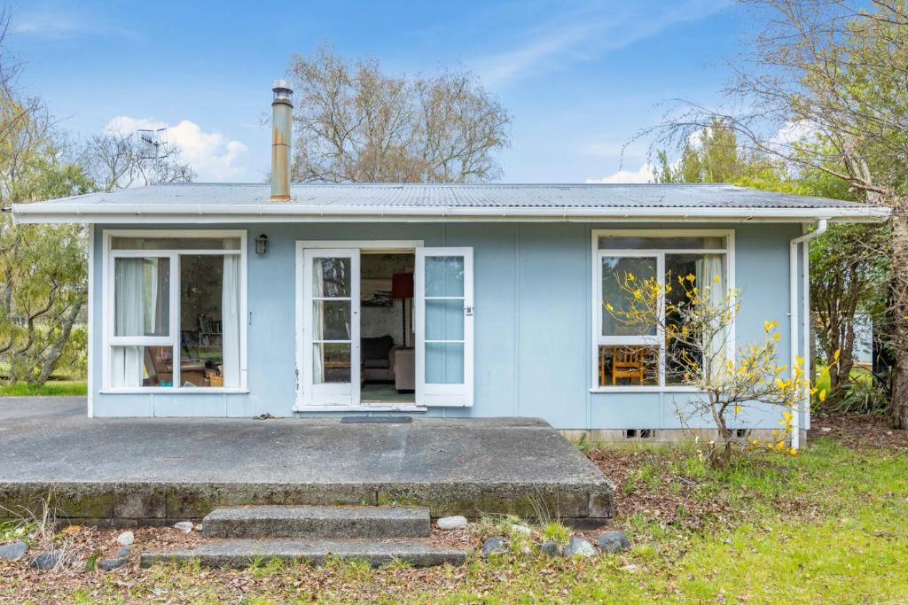 Cette maison bleue est dotée de fenêtres blanches et d'une terrasse couverte. dans l'établissement Cedar Cottage - Tauranga Taupo Holiday Home, à Kuratau