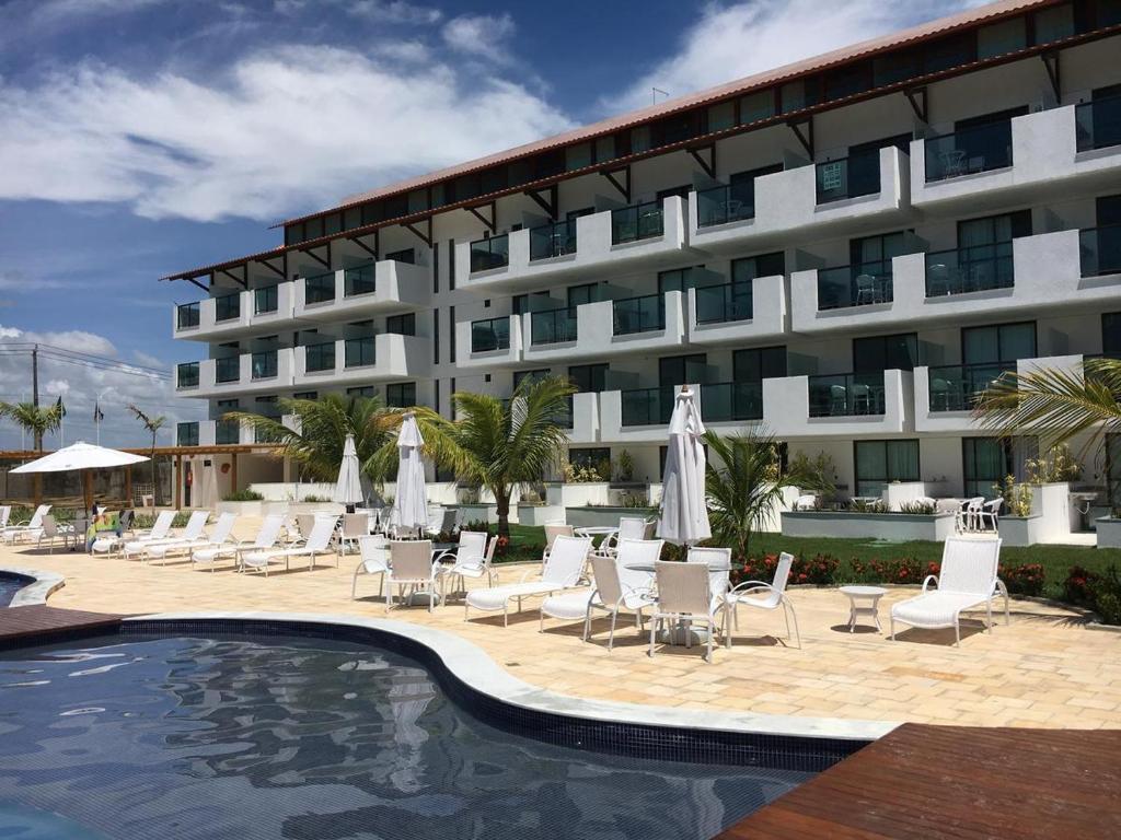 un hotel con piscina y sillas y un edificio en LAGUNA BEACH FLAT EM PORTO en Porto De Galinhas