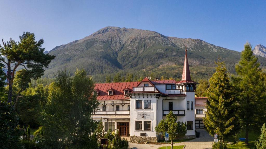 a large white house with a mountain in the background at Villa Dr Szontagh Est. 1876 in Vysoke Tatry - Novy Smokovec