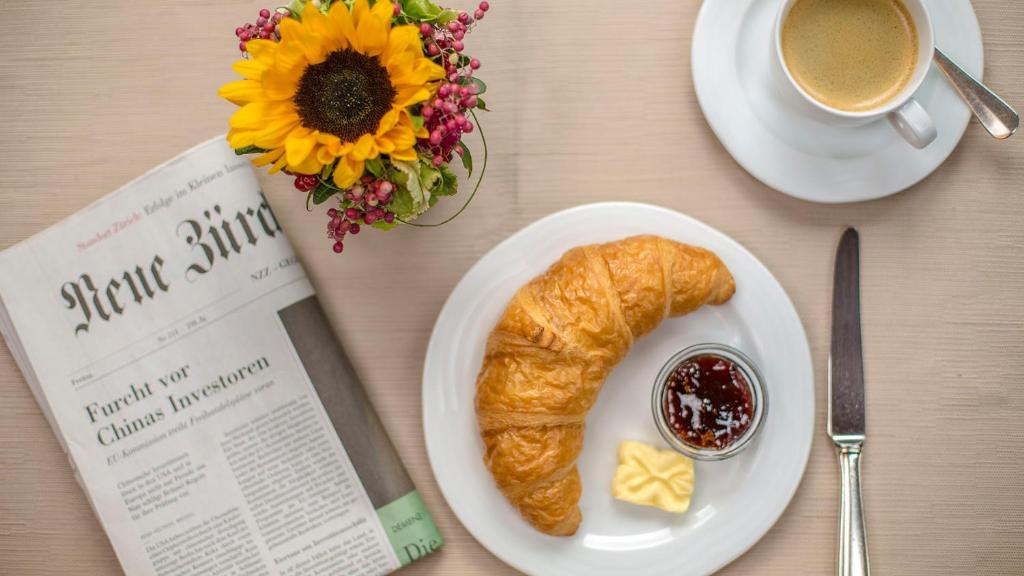 a plate with a croissant and a cup of coffee and a book at Alpenblick in Zermatt