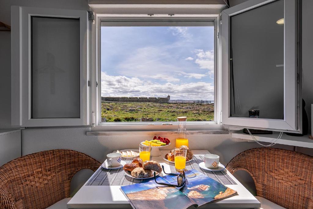 a table with breakfast food and a window with a view at CASA DA FALÉSIA 28 - Estúdio in Peniche
