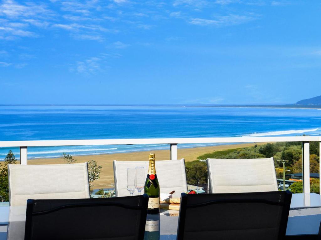 a bottle of wine sitting on a table with chairs and the ocean at Jewel of Gerroa Gerroa in Gerroa