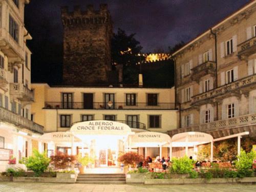 Un bâtiment avec des personnes assises devant lui la nuit dans l'établissement Hotel Croce Federale, à Bellinzone