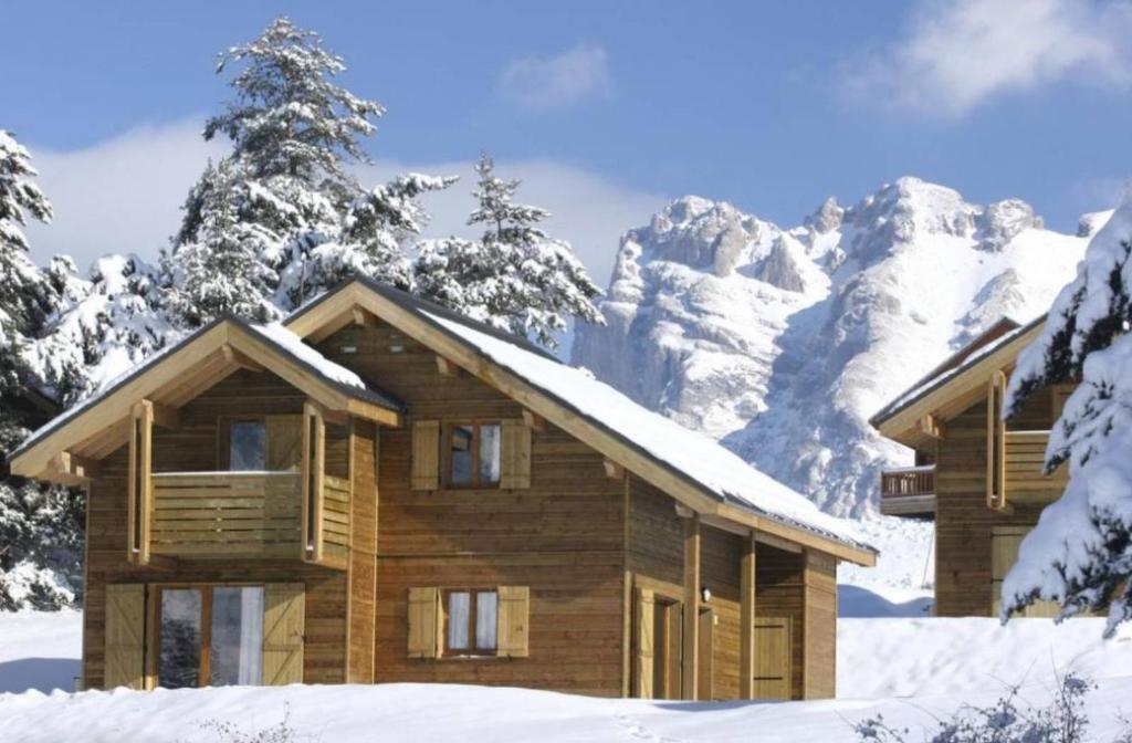 une cabane en rondins dans la neige avec des montagnes enneigées dans l'établissement Residence La Crete du Berger - maeva Home, à La Joue du Loup