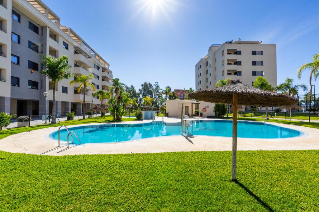 a large swimming pool with an umbrella and grass at Apartamento Playa Marinsa in Torre del Mar