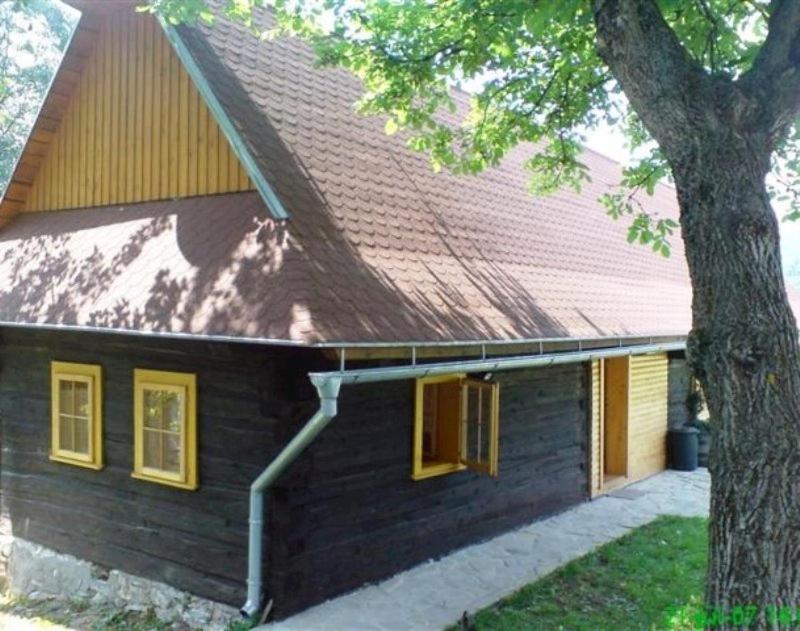 ein schwarzes Haus mit gelben Fenstern und einem Baum in der Unterkunft Chata pod Orechom in Terchová