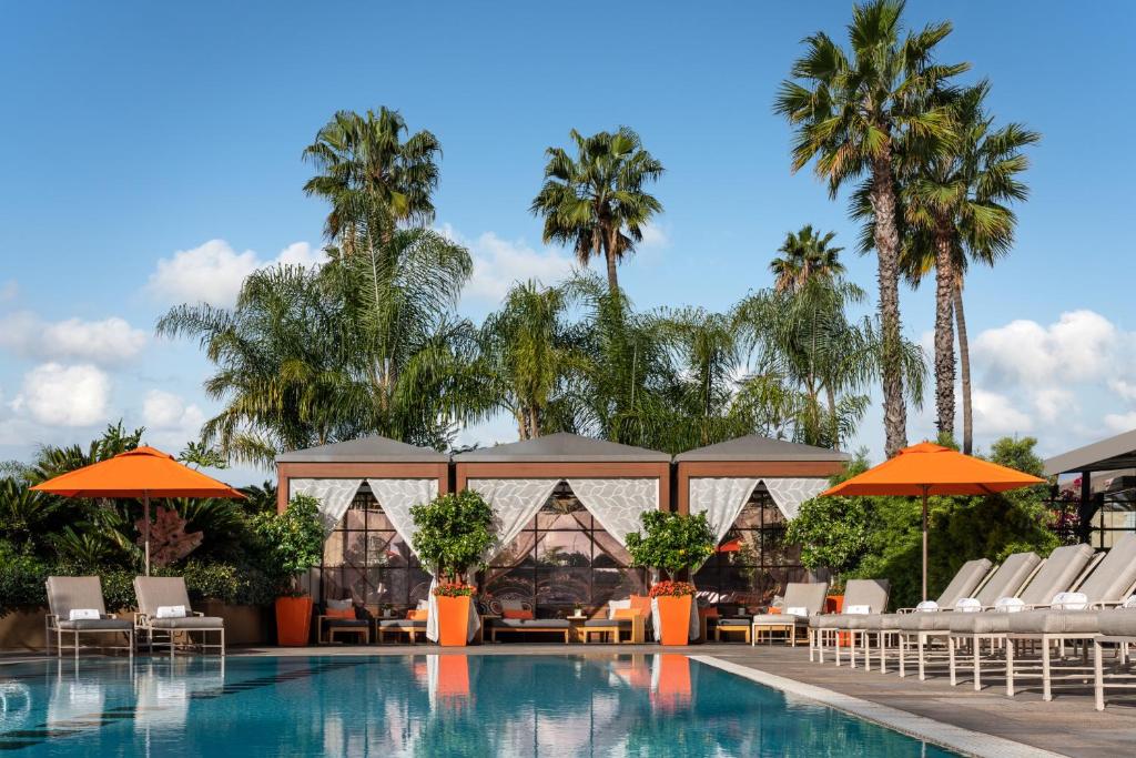 - une piscine avec chaises longues, parasols et palmiers dans l'établissement Four Seasons Hotel Los Angeles at Beverly Hills, à Los Angeles