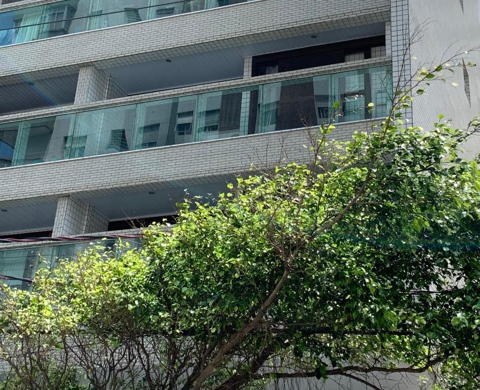 un edificio alto con un árbol delante de él en Apartamento Pé na Areia - Santos, en Santos