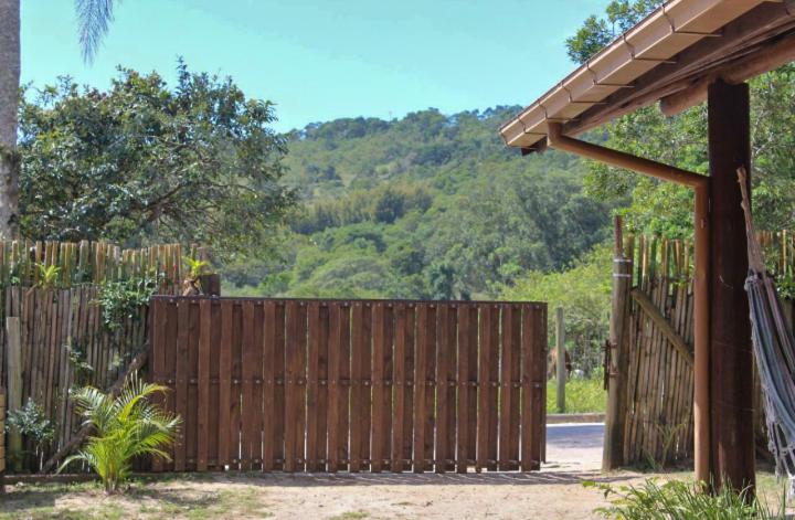 uma cerca de madeira com um portão em frente a uma montanha em Boa Vibe Complexo Rosa Norte na Praia do Rosa