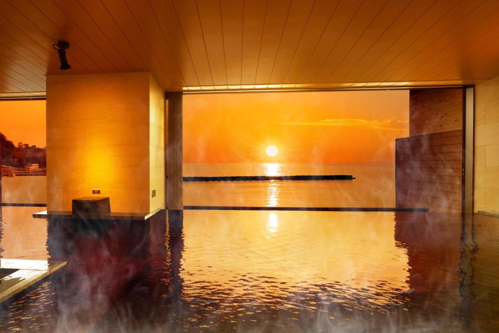 a pool of water in a gym with the sun setting at Ooedo Onsen Monogatari Toi Marine Hotel in Izu