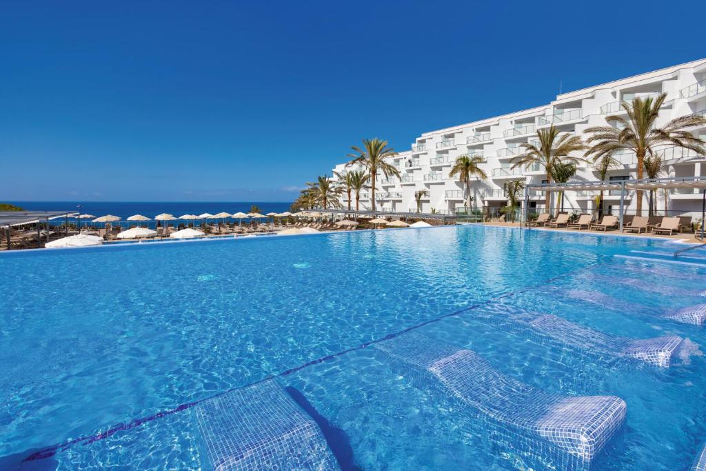 a large swimming pool with chairs in front of a hotel at Hotel Riu Buenavista - All Inclusive in Adeje