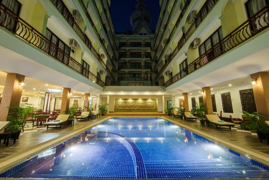 Smiling Deluxe Hotel في سيام ريب: حمام سباحة داخلي في الفندق مع الكراسي والطاولات