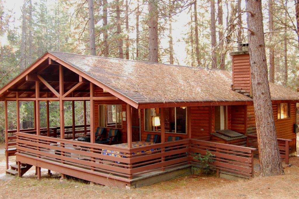 a log cabin with a large porch in the woods at 84 Hastings Hideaway in Wawona