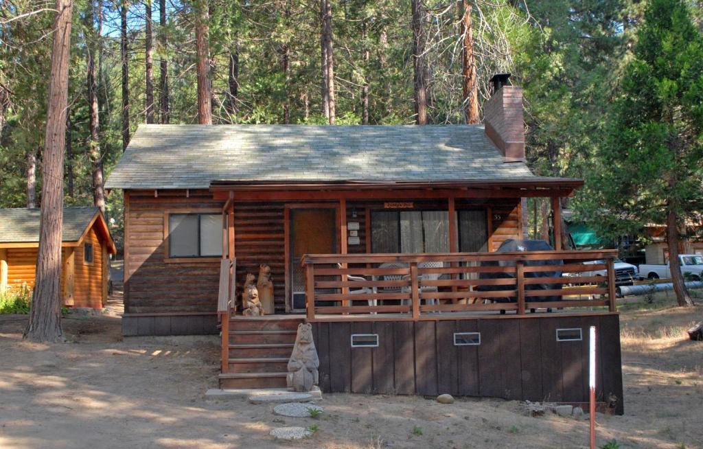 a cabin in the woods with a cat sitting on the porch at 35 Cubbys Den in Wawona