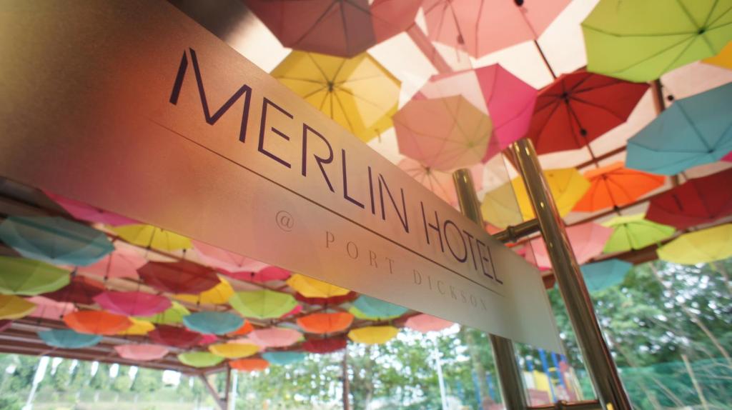 Um sinal que diz "Merlin Room" debaixo de um monte de guarda-chuvas. em Merlin Hotel em Porto Dickson