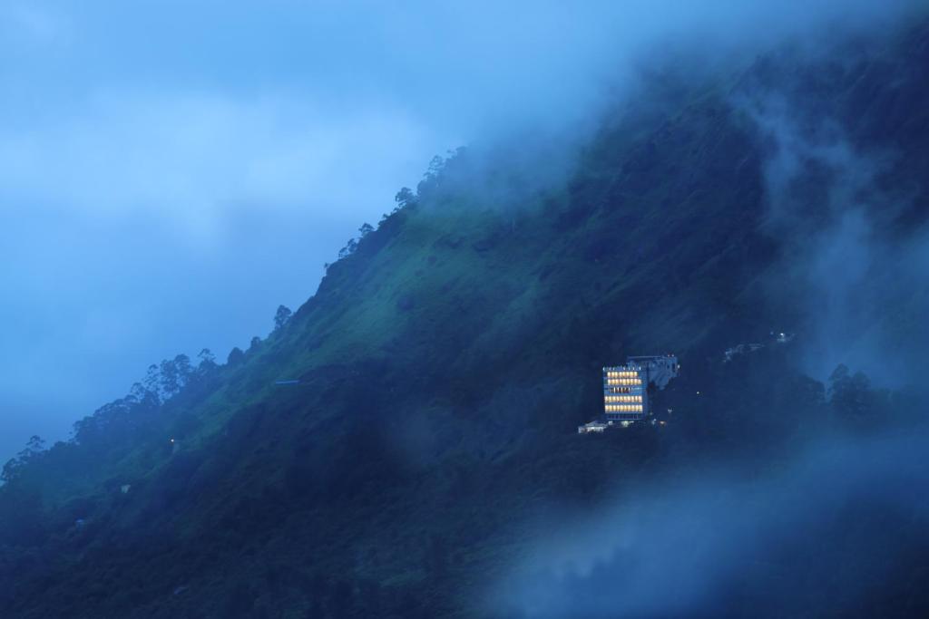 a misty mountain with a building on the side of it at Amber Dale Luxury Hotel & Spa, Munnar in Munnar