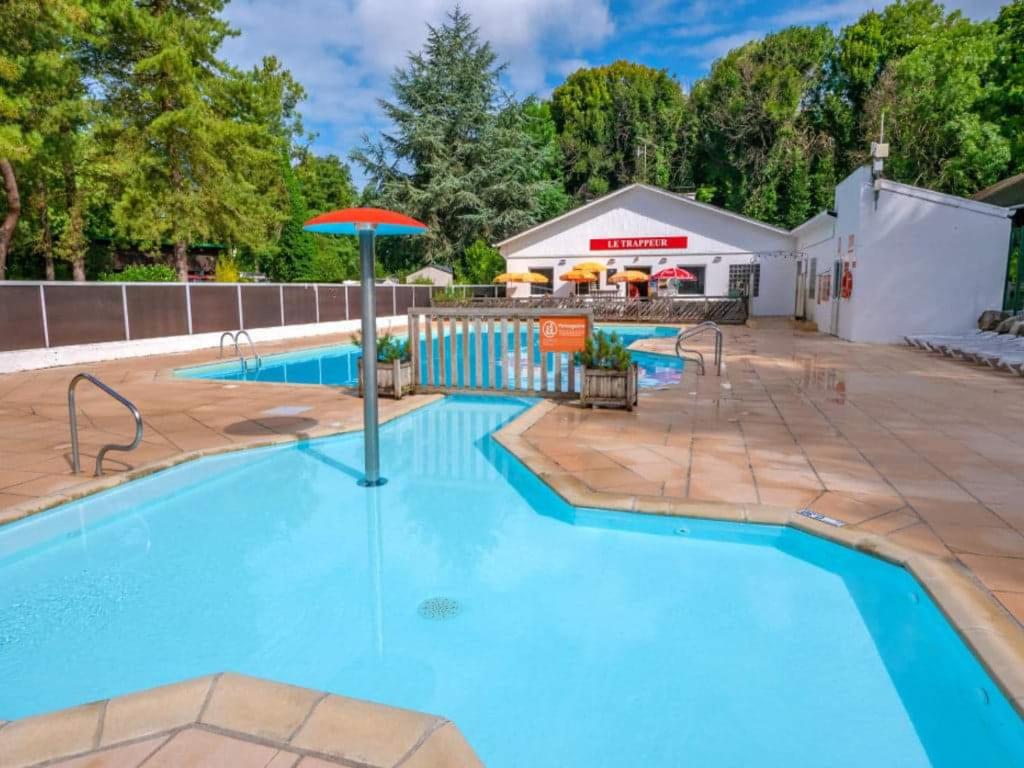 a swimming pool with an umbrella next to a building at LE ILÔ - camping la dune blanche in Camiers