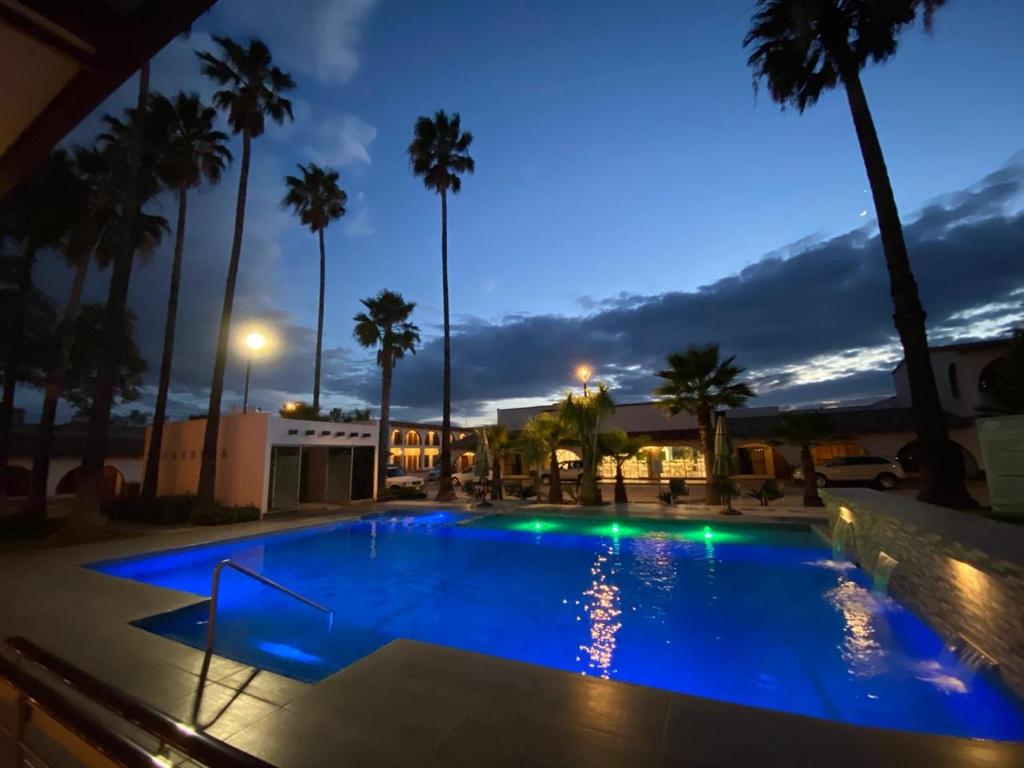 a swimming pool at night with palm trees at Hotel Sand´s San Luis in San Luis Potosí